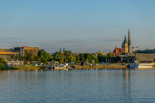Wide panoramic view of a riverfront city skyline with church spires in clear evening light reflecting on the water.