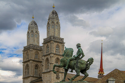 Cathedral towers behind an equestrian statue under cloudy skies.
