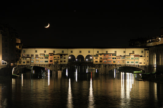 Historic bridge at night with a crescent moon and reflections.