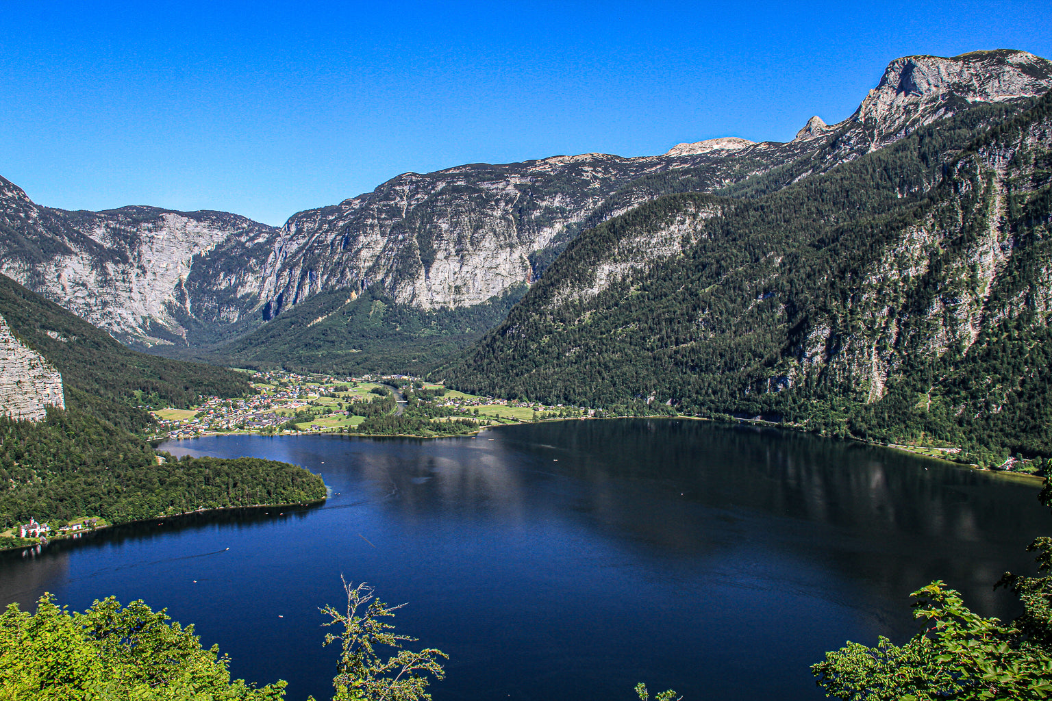 Wide view of a blue mountain lake with steep cliffs and a village lining the shoreline.