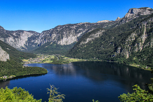 Wide view of a blue mountain lake with steep cliffs and a village lining the shoreline.