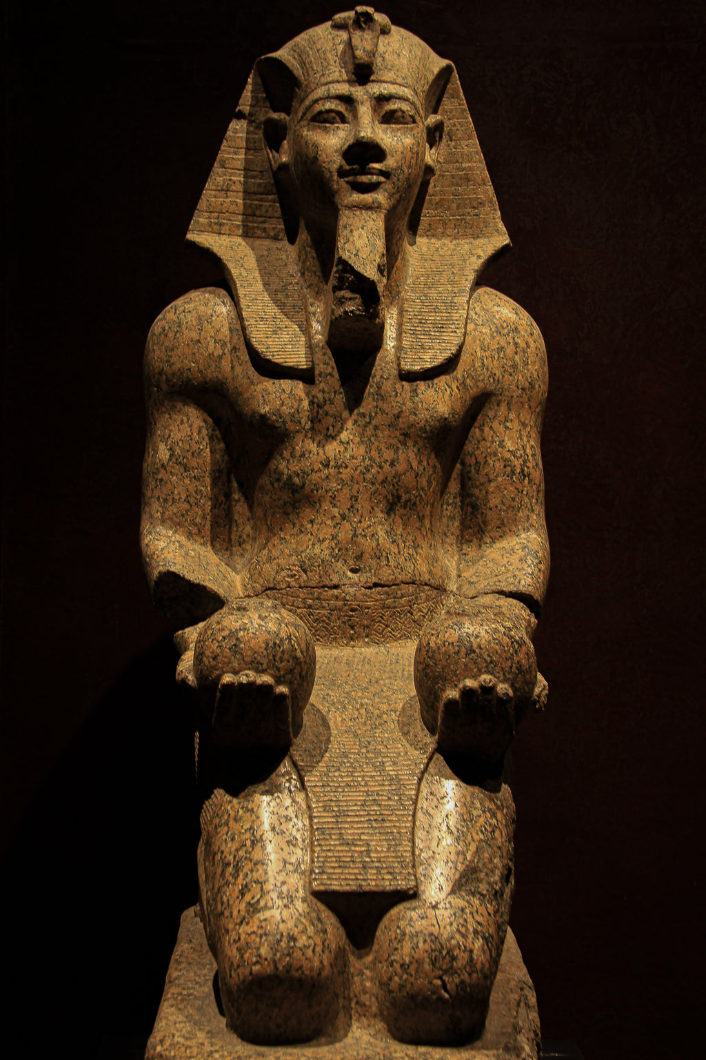 Seated pharaoh statue photographed against a dark background.