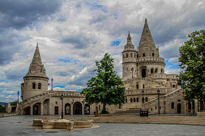Historic stone towers and arches in a courtyard beneath a dramatic, cloud-filled sky.