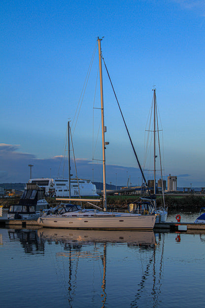 Sailboat docked in a marina at dusk with reflections in the water.