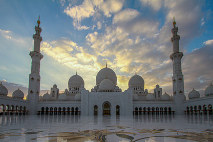 Symmetrical view of a white domed mosque with minarets beneath a dramatic sunset sky.