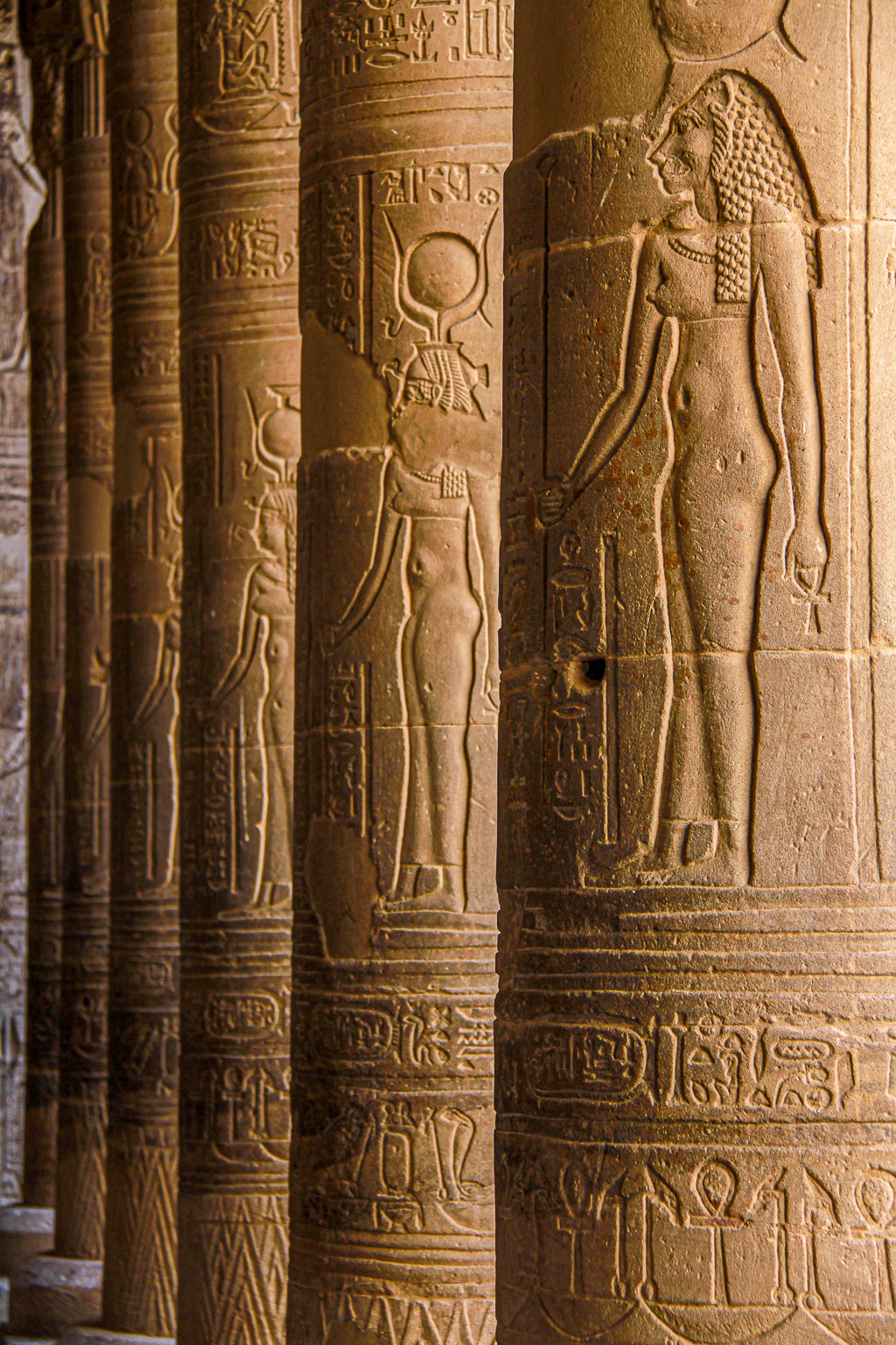 Ancient Egyptian temple columns carved with hieroglyphs and relief figures in warm sunlight.