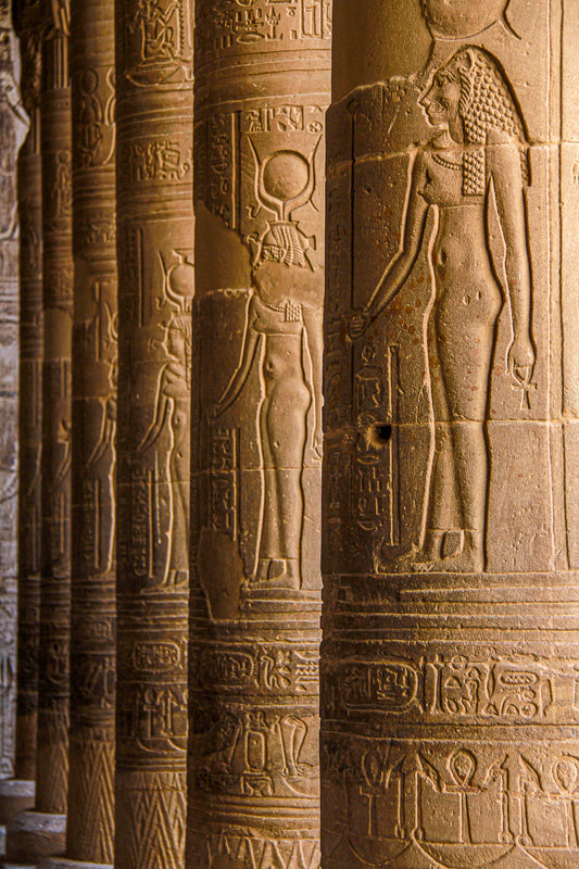 Ancient Egyptian temple columns carved with hieroglyphs and relief figures in warm sunlight.