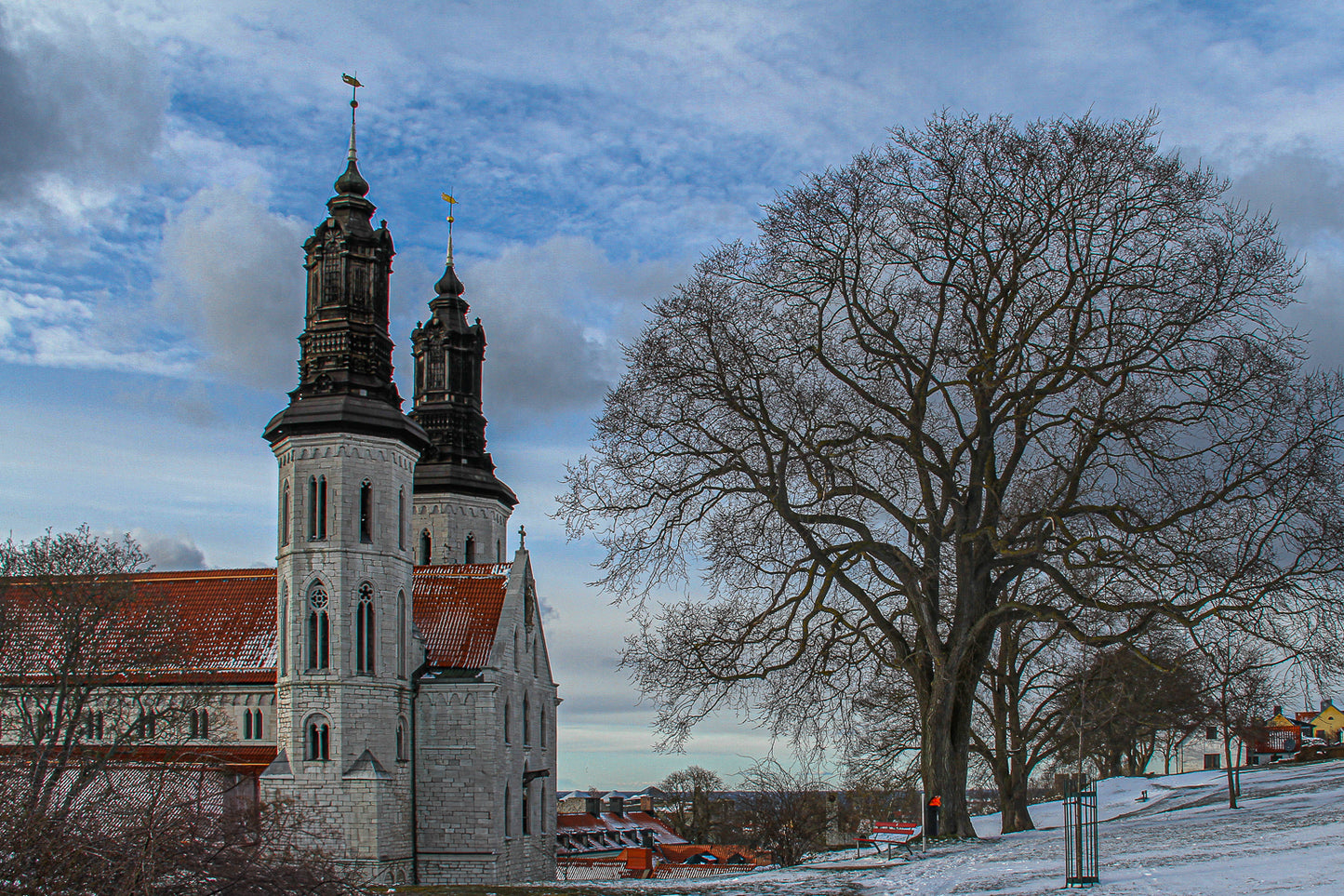 Twin-towered church beside a large bare tree in winter snow.