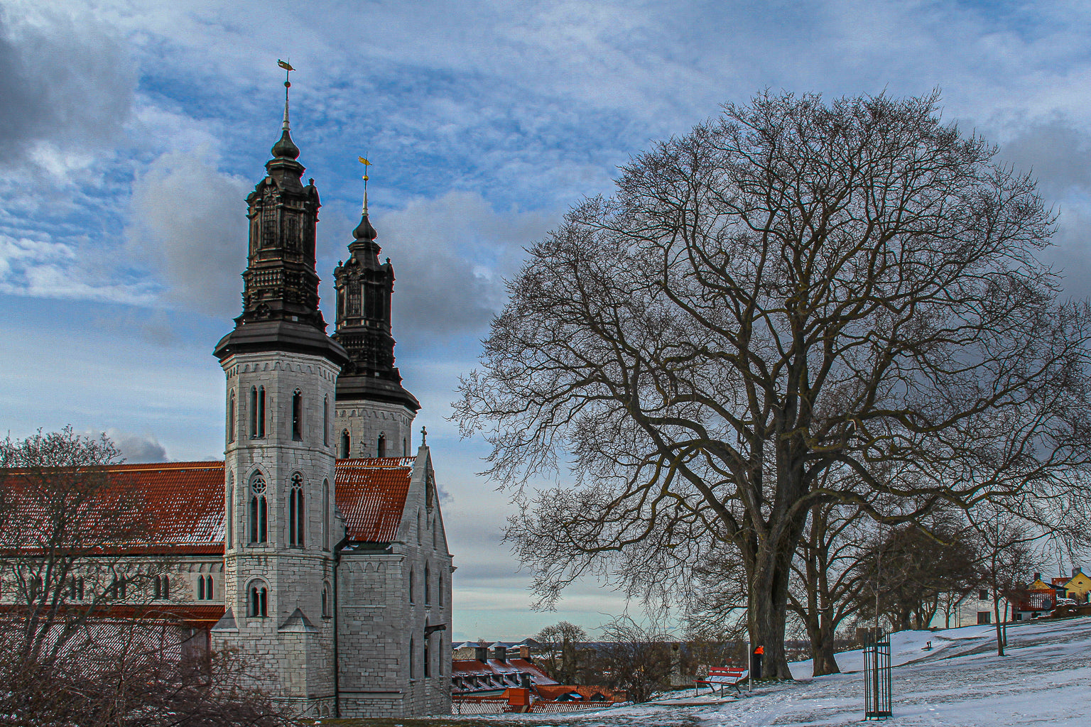 Twin-towered church beside a large bare tree in winter snow.