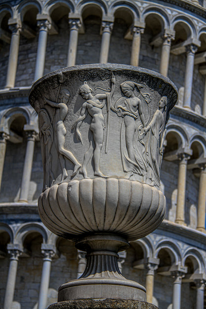 Carved stone urn with classical figure relief in front of arched columns.